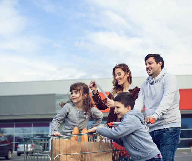 Cheerful family going back from supermarket. Pushing shopping cart and carrying shopping bags. Mother looking at shop bill.